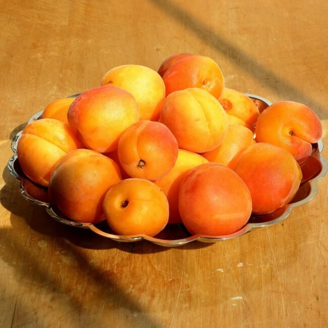A vibrant pile of fresh apricots on a metal plate enhances any summer dining setting.