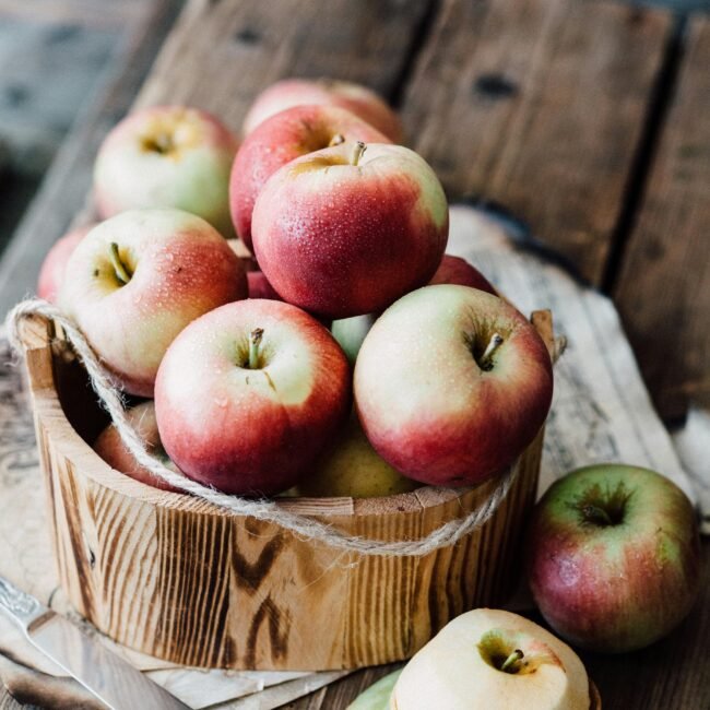 A close-up of ripe apples in a wooden basket on rustic planks. Ideal for fall harvest themes.